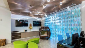 Un espace de bureau moderne doté d’un plafond en bois, de sièges verts, d’un grand téléviseur et d’un mur en verre orné d’un motif géométrique.