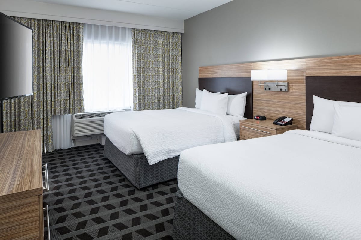 A hotel room with two beds, a TV, a bedside table with a phone, and a window with curtains.