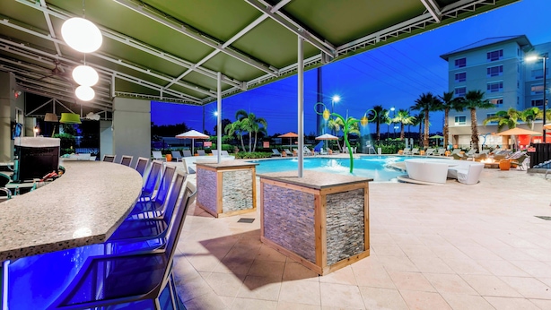 Un espace piscine extérieur comprenant un bar, des chaises longues et des parasols.