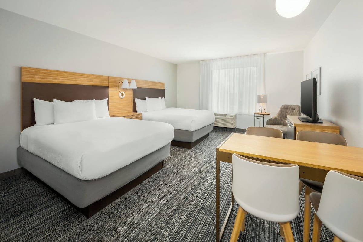 Een hotelkamer met twee bedden, een bureau, een stoel, een televisie en een raam met gordijnen.