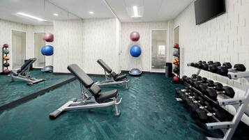 A gym with exercise equipment, a mirror, and a television on the wall.