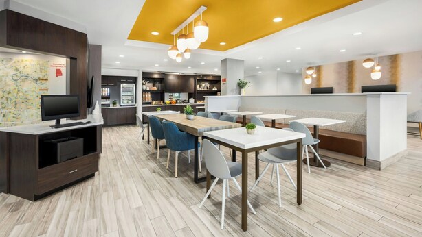 Een moderne hotellobby met een receptiebalie, een zithoek en een kaart aan de muur.