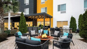 Een terras buiten met wicker meubels, een vuurkuil in het midden en een overdekte zithoek.