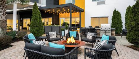 An outdoor patio with wicker furniture, a central fire pit, and a covered seating area.