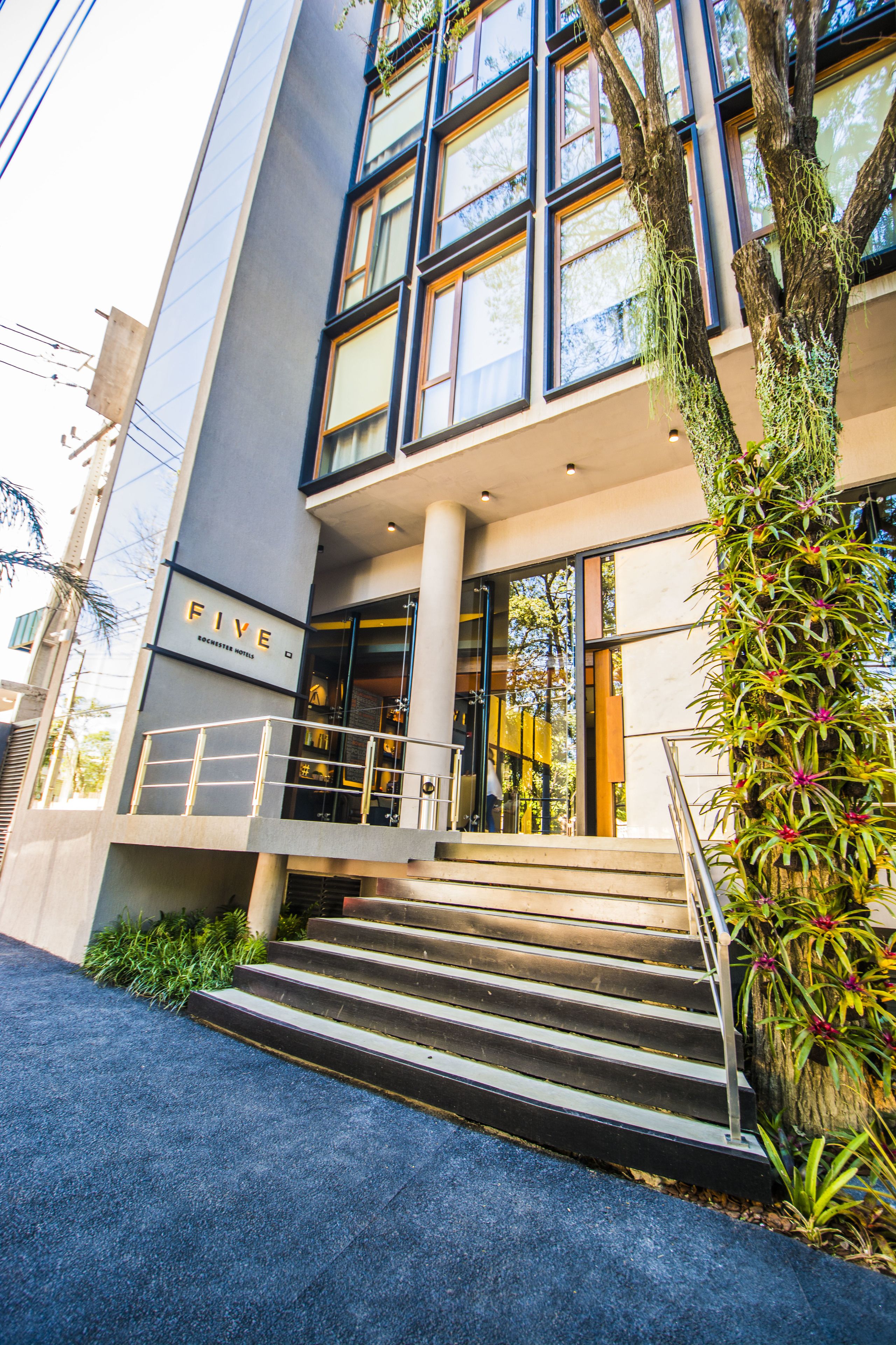 Une entrée d’hôtel moderne avec un escalier menant à l’entrée, une enseigne indiquant « FIVE », et un jardin vertical sur le côté droit.
