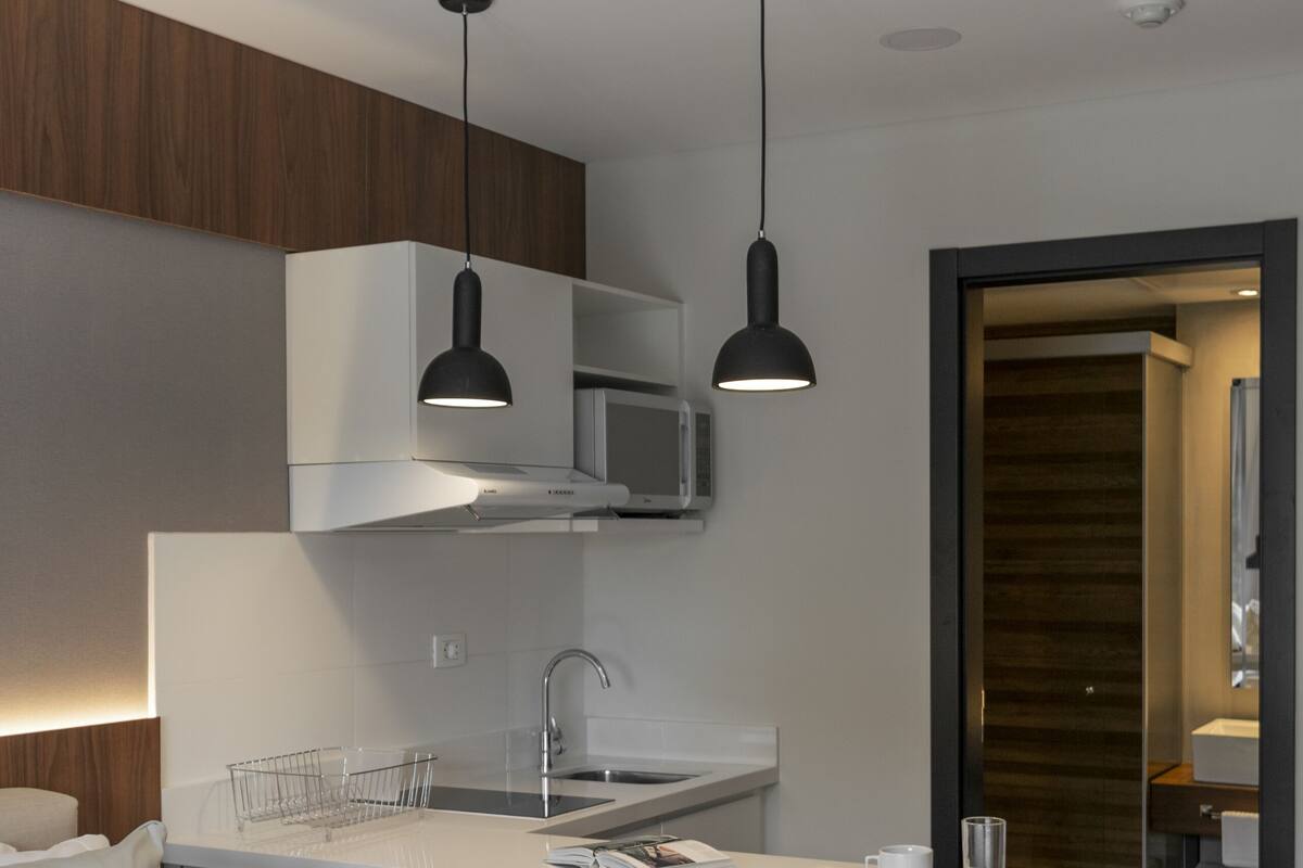 A modern hotel room with a kitchenette, a bed, and a small dining area.
