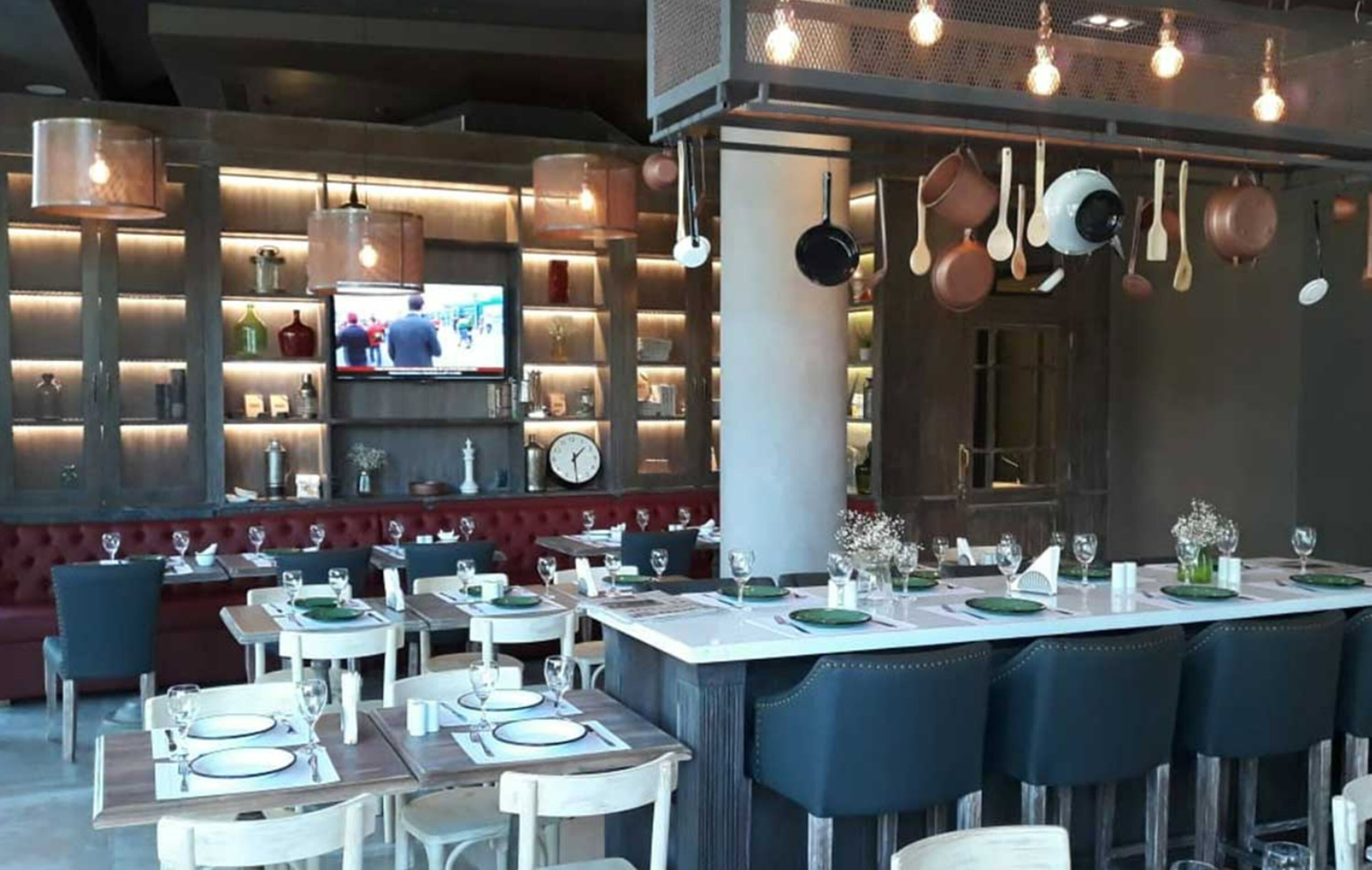 A restaurant with a bar area, tables set for dining, and hanging pots and pans.