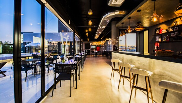 A modern restaurant interior with large windows, bar area, and seating arrangements. - Five Hotel & Residences (Asunción)