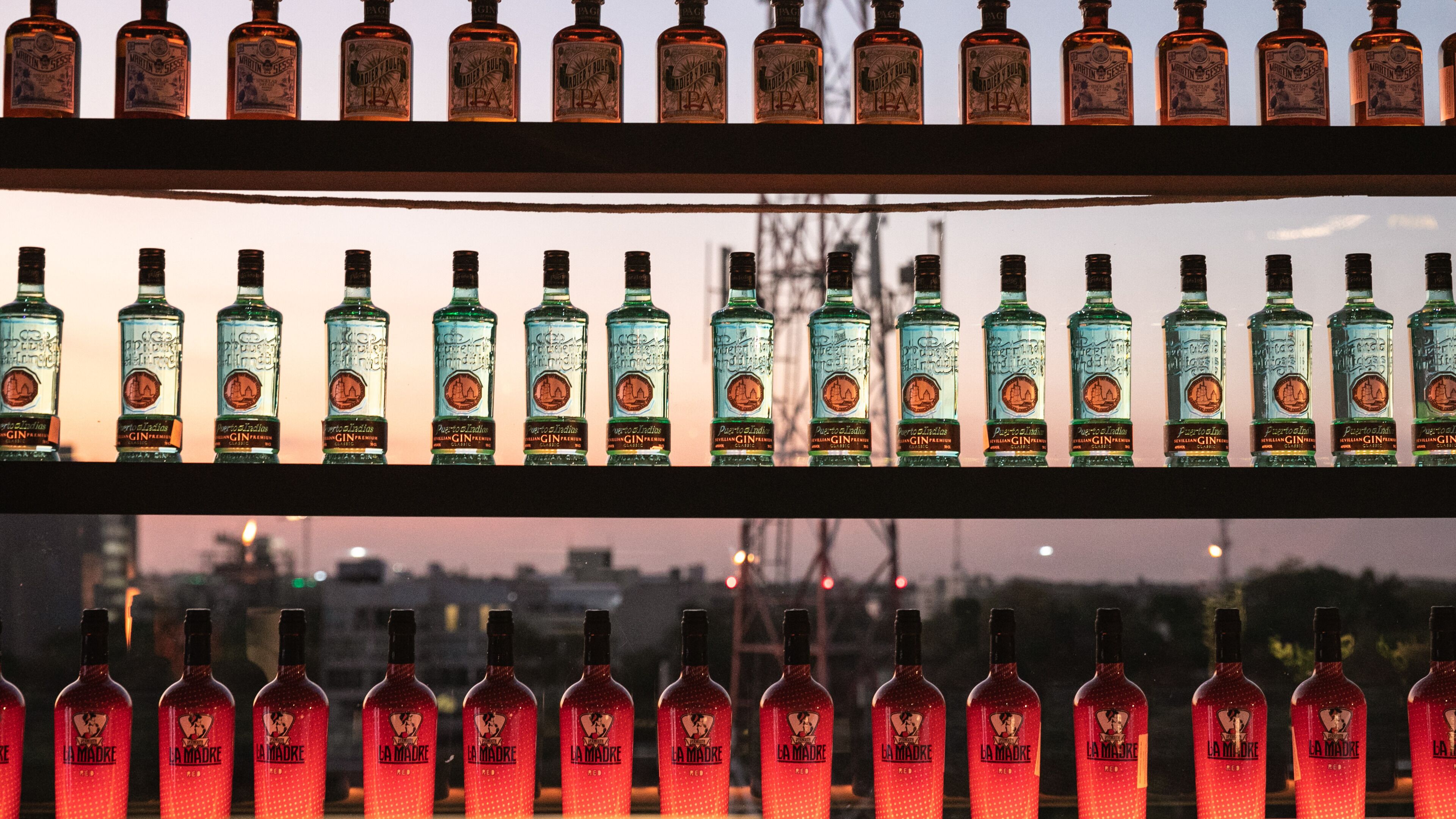 Bottles of alcohol arranged on shelves, with a cityscape in the background.