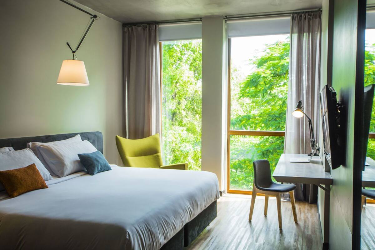 A hotel room with a bed, a desk, a chair, a lamp, and a TV.