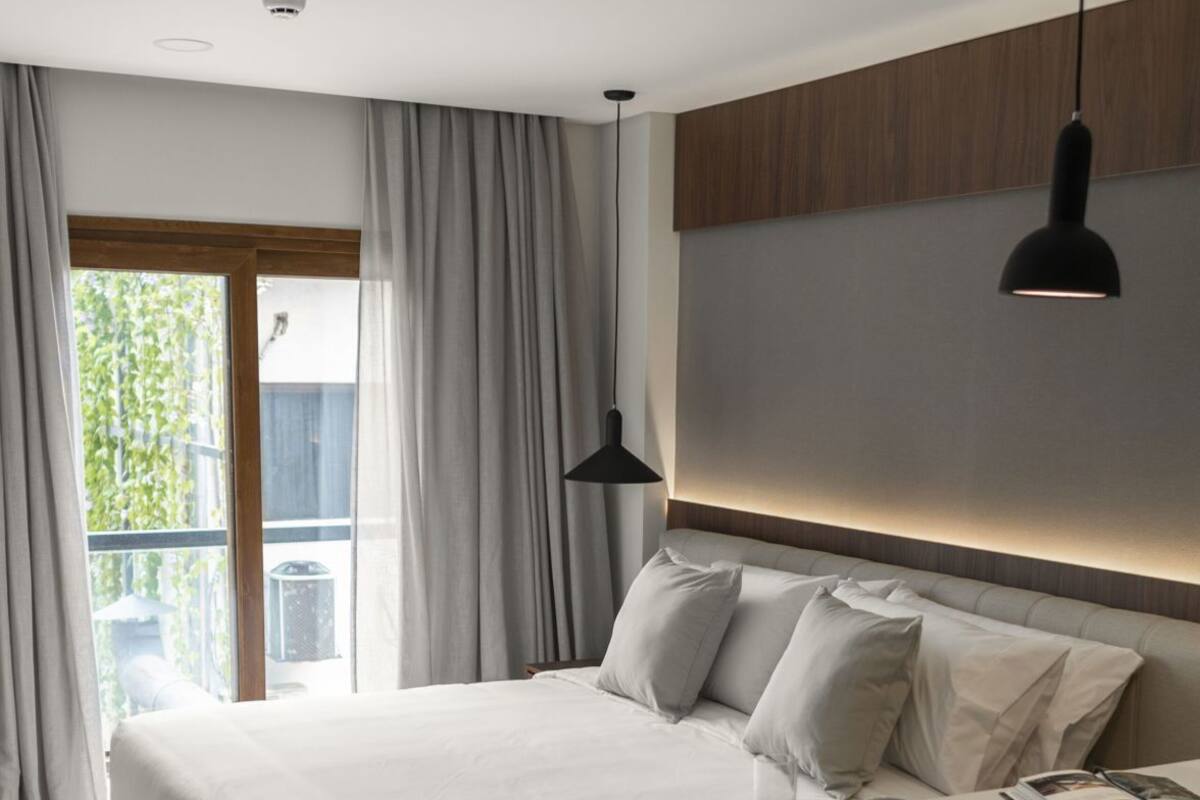 A modern hotel room with a bed, bedside table, and a desk with a chair.