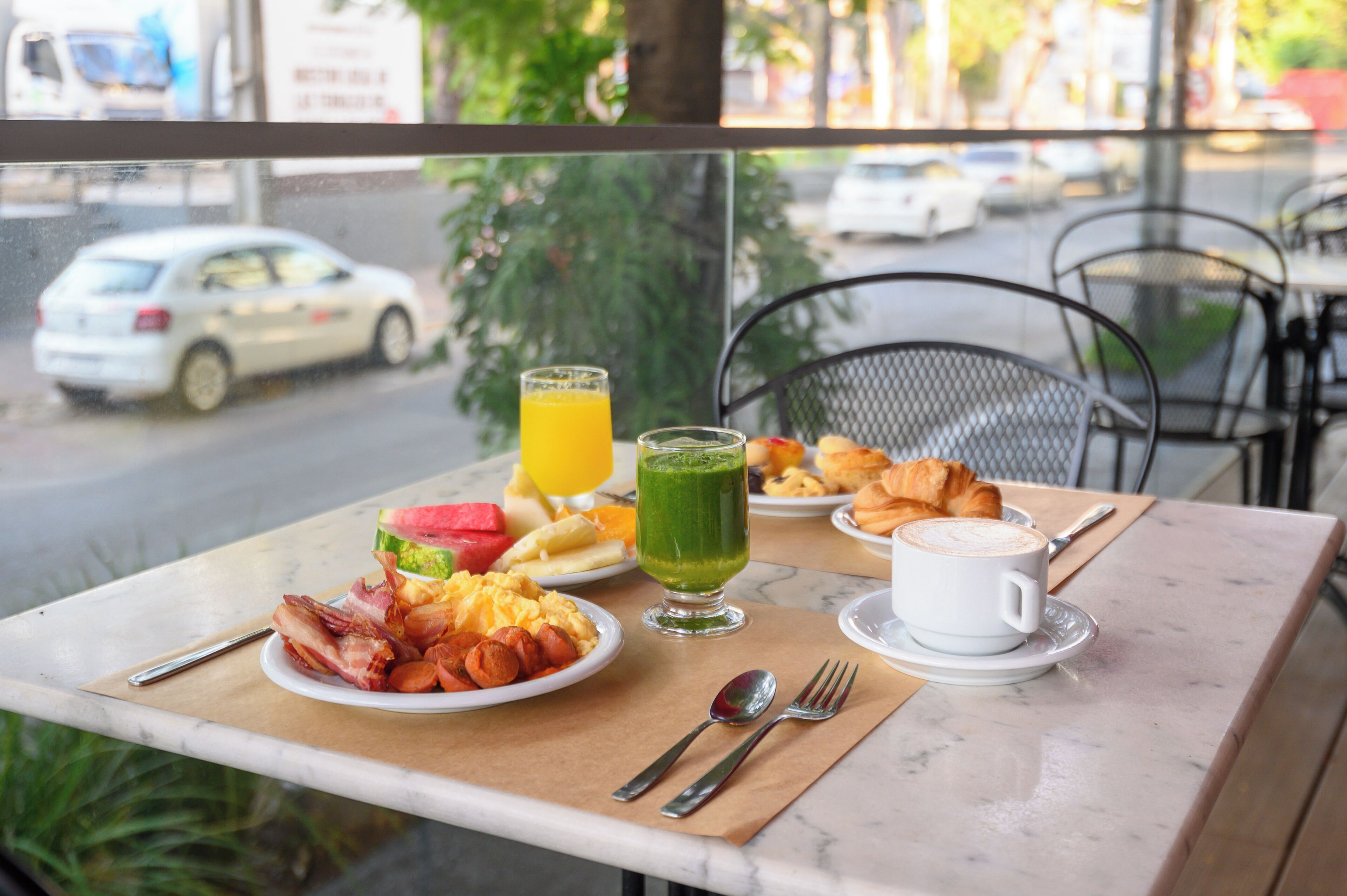 A breakfast table with plates of food, a glass of orange juice, a green smoothie, croissants, and a cup of coffee.