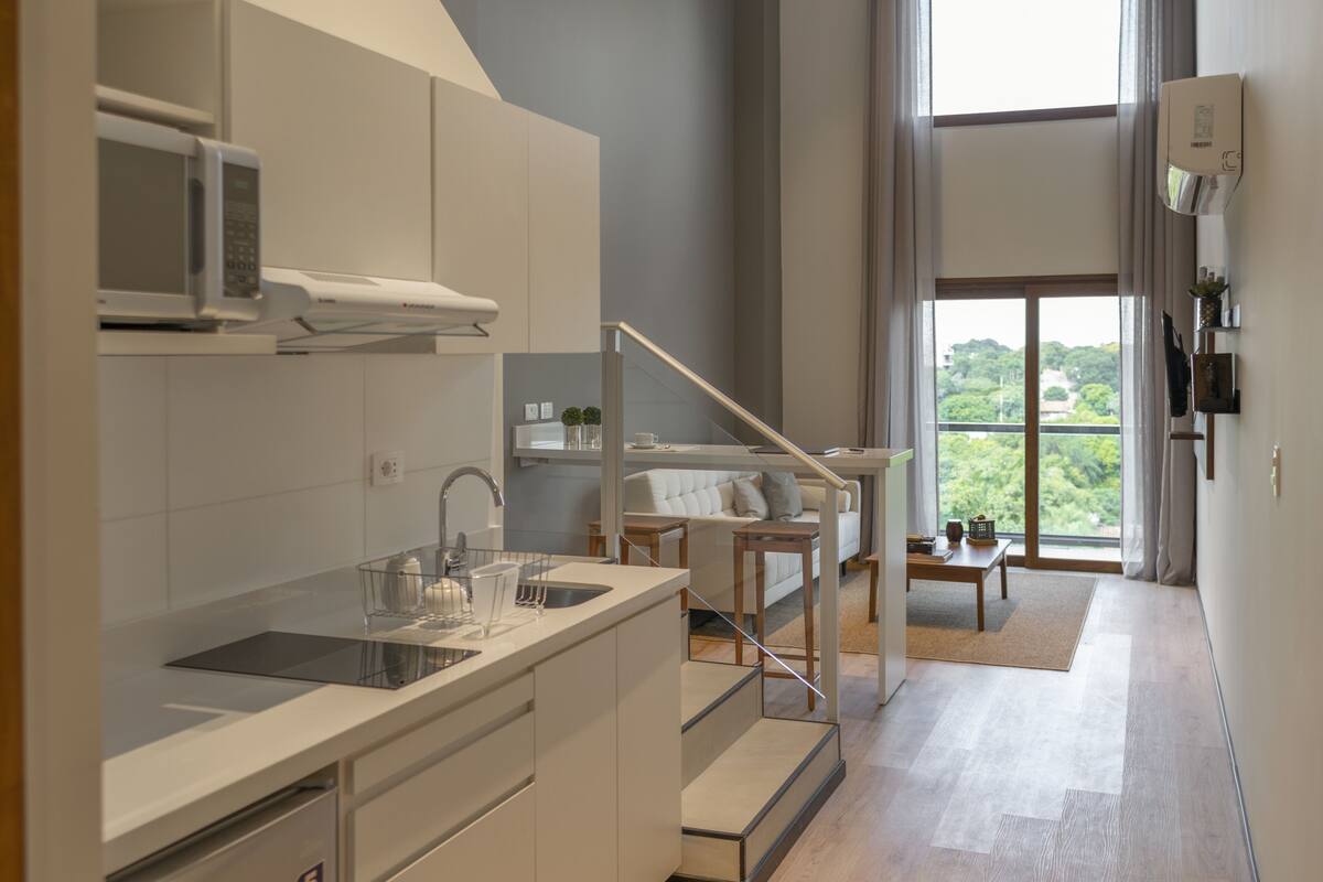 A modern kitchen with a built-in microwave, a sink, and a staircase leading to a living area with a sofa and a table.