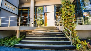 A modern hotel entrance with a staircase leading to the lobby, surrounded by greenery and a glass facade. - Five Hotel & Residences (Asunción)