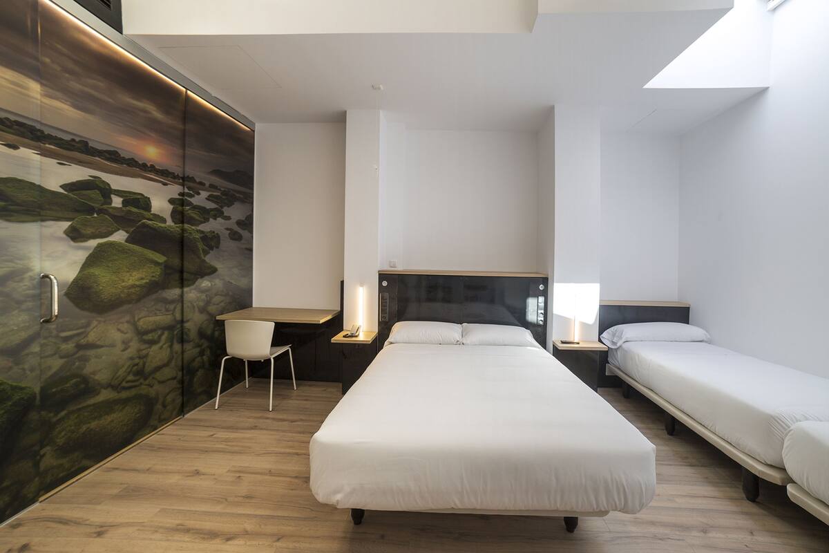 Une chambre d’hôtel avec un grand lit, deux petits lits, un bureau et une chaise.