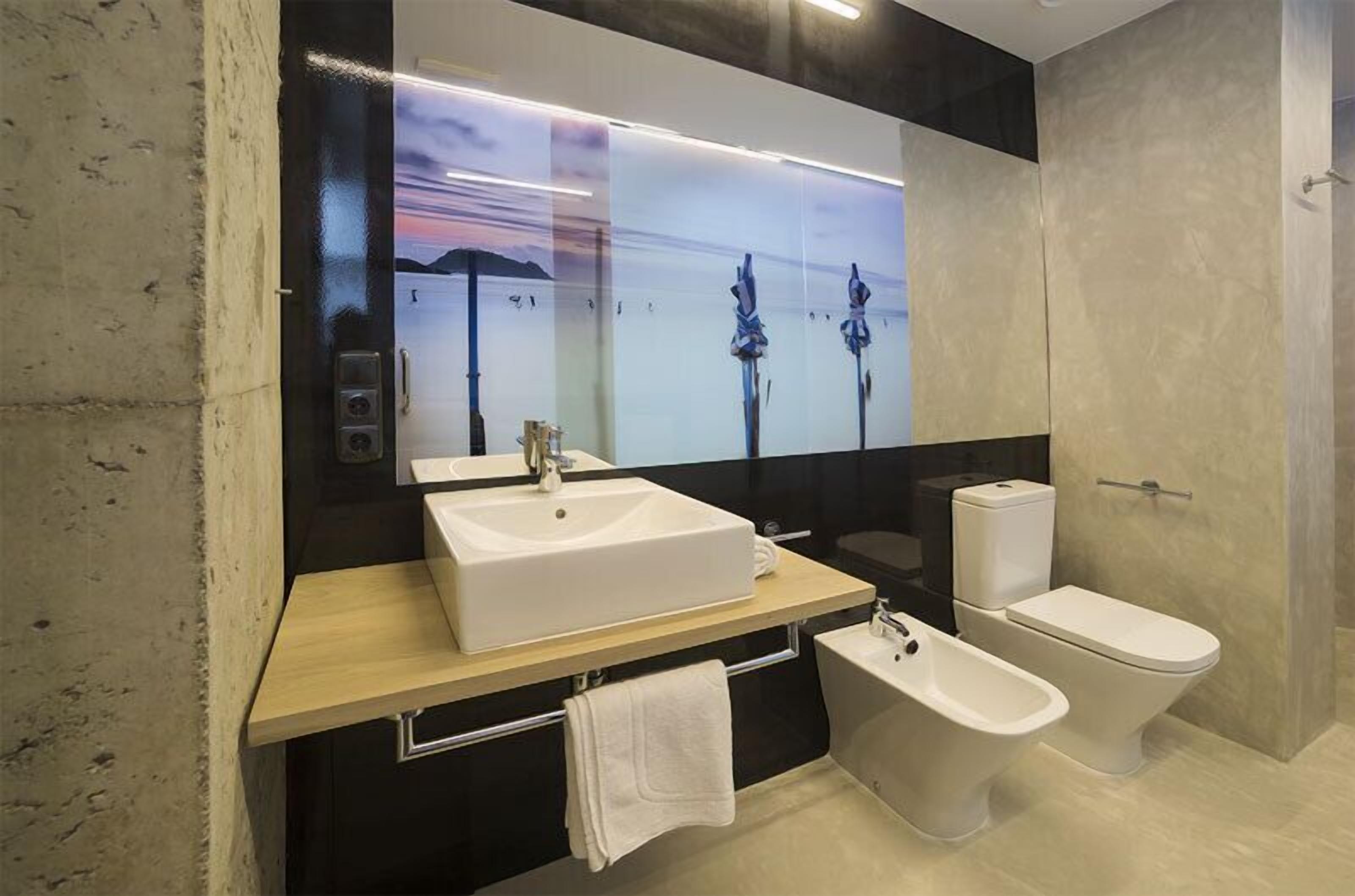 A modern bathroom with a large mirror, a white sink, a toilet, and a bidet.