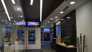 A modern interior with glass doors leading to a retail area, a reception desk with a plant, and a wall-mounted sculpture. - Hotel Zerupe (Zarautz)