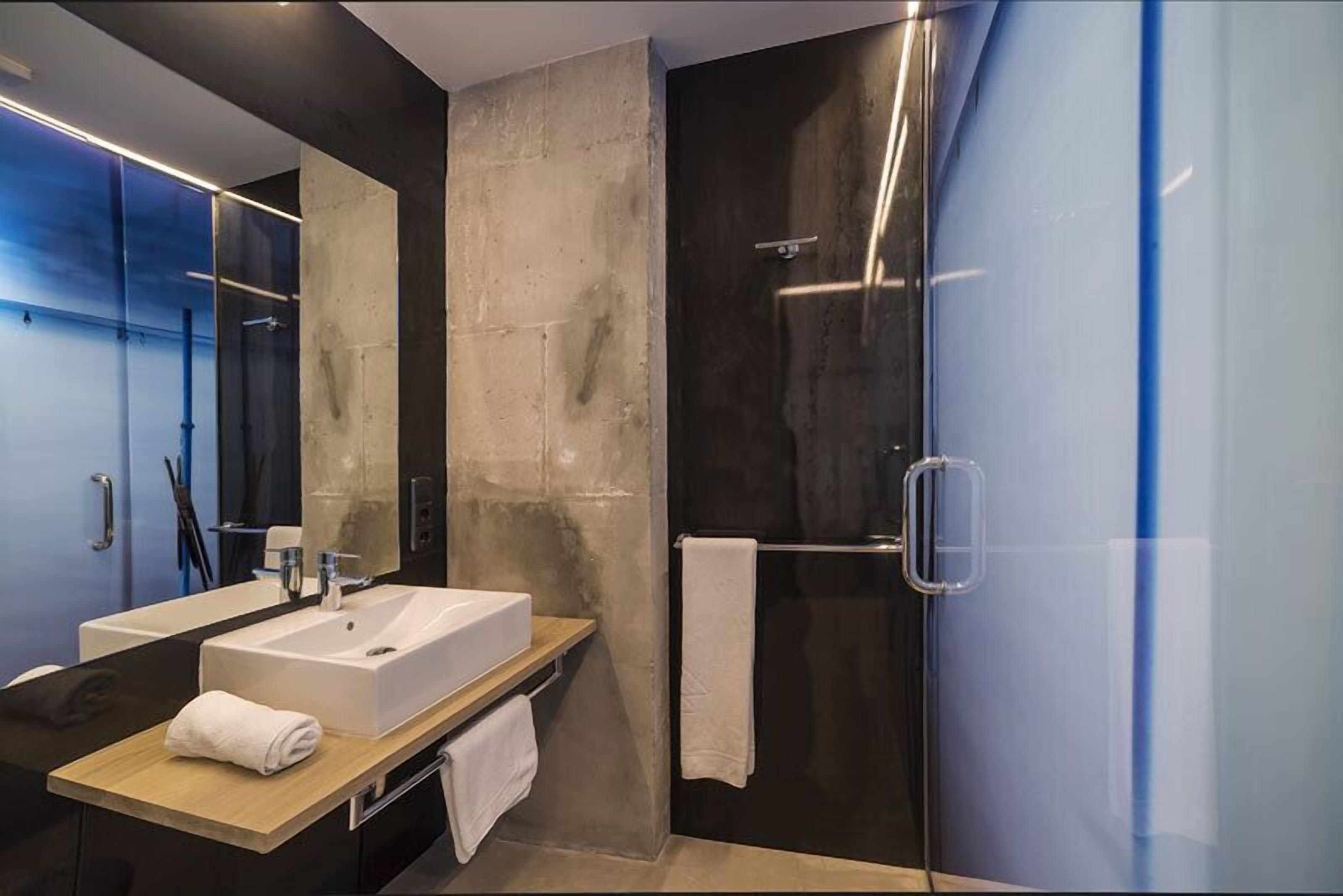 A modern bathroom with a large mirror, a white sink, and a glass shower enclosure.