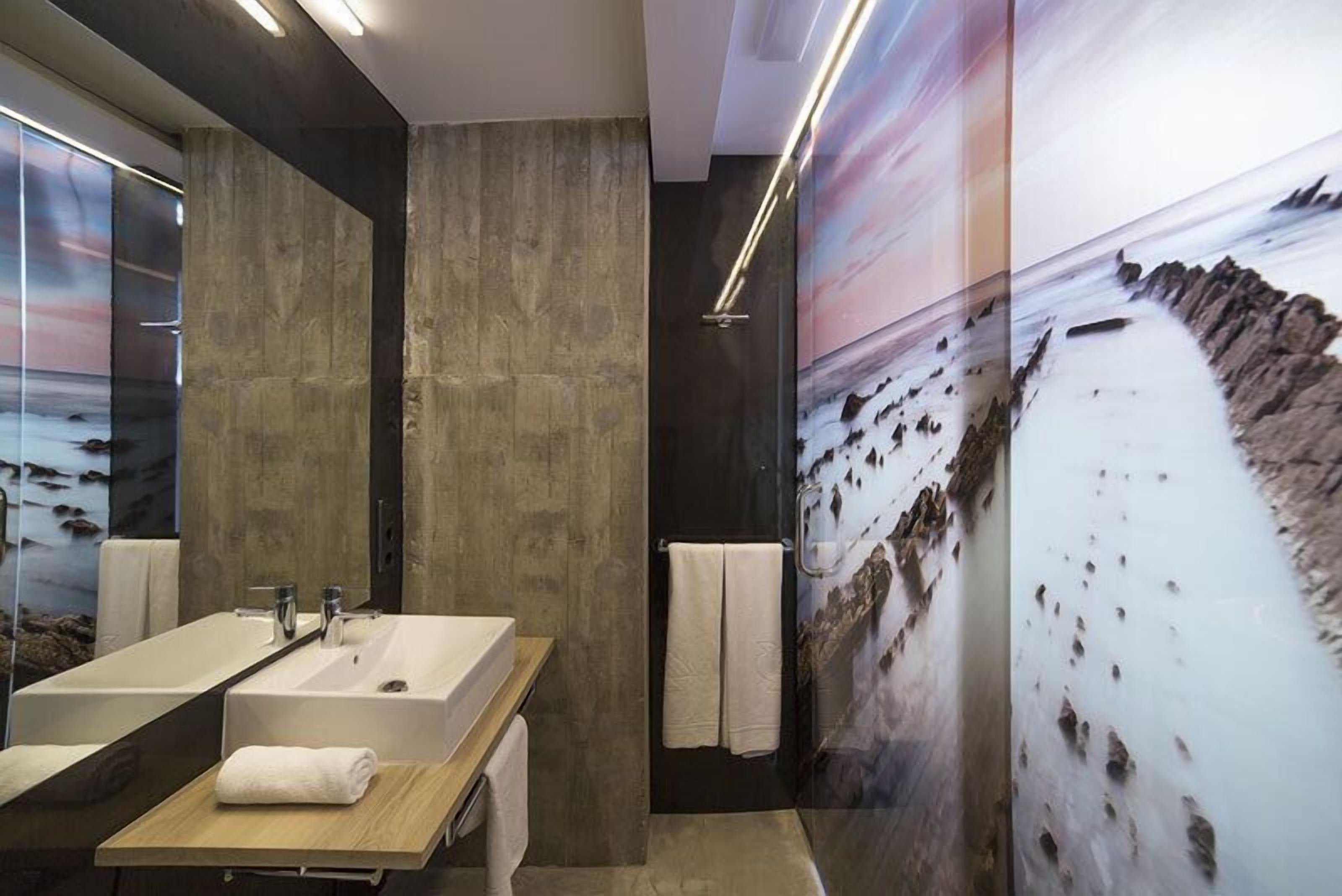 Une salle de bain moderne avec un grand miroir, deux lavabos et une douche.