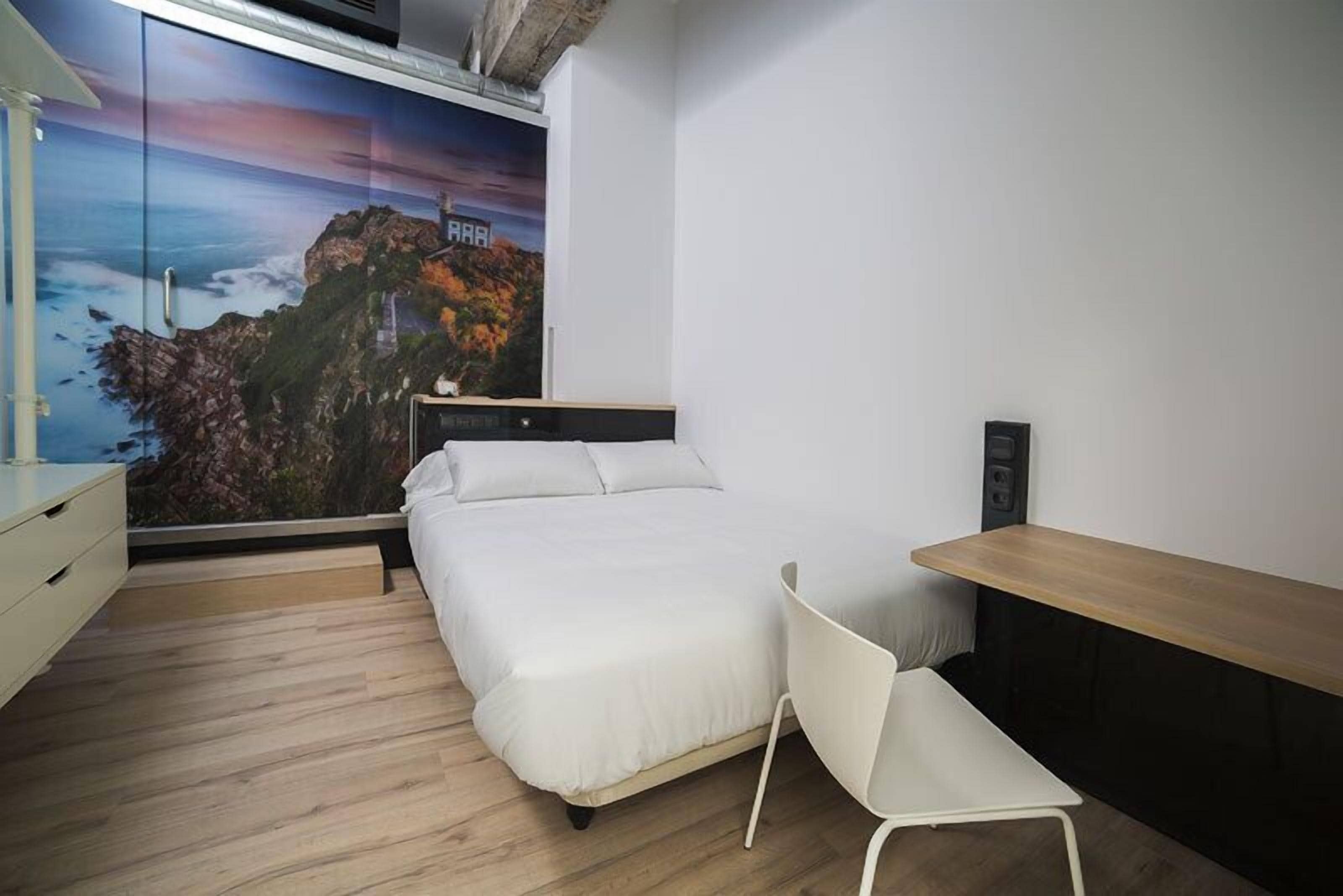 Ein Schlafzimmer mit einem Bett, einem Schreibtisch, einem Sessel und einem großen Fenster mit schöner Aussicht.