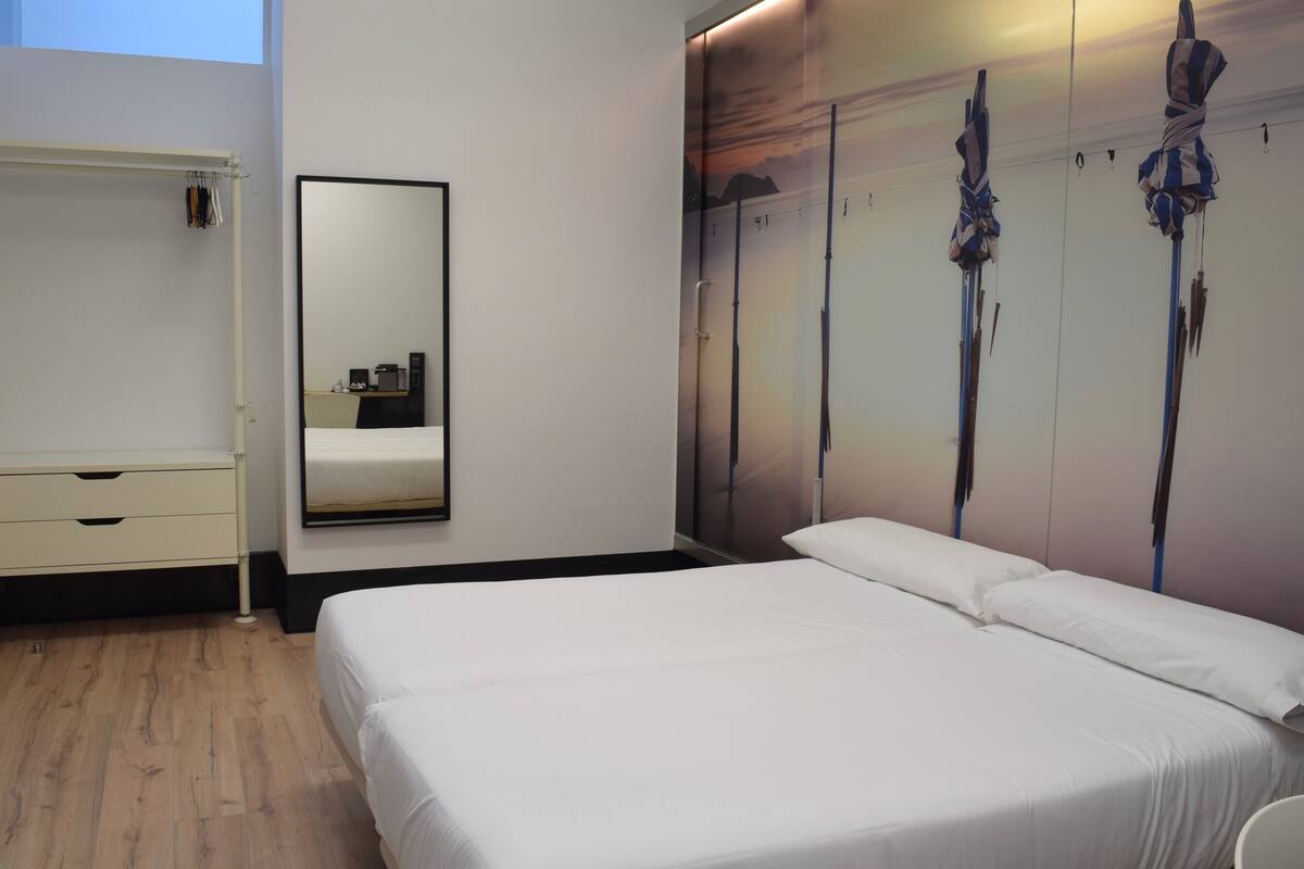 Une chambre d’hôtel équipée d’un lit, d’une commode, d’un miroir et d’un mur orné d’une fresque représentant un paysage.