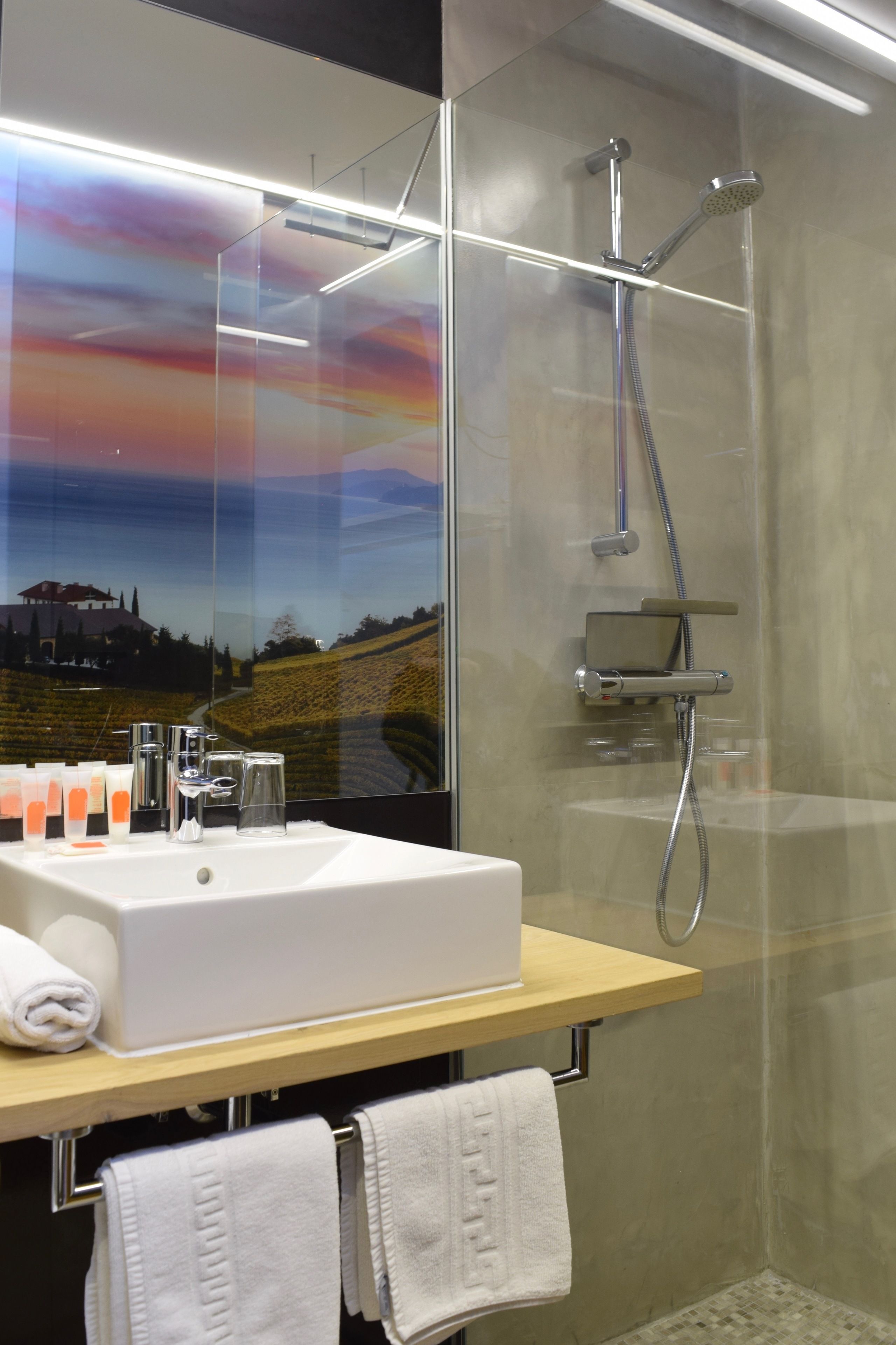 Een moderne badkamer met een douchecabine van glas, een wit wastafelmeubel met een houten blad en een grote spiegel die uitzicht geeft op een mooi landschap.