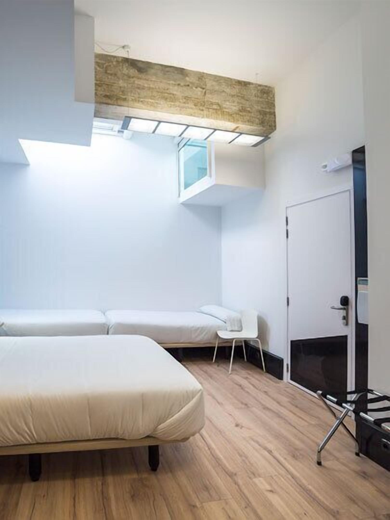 Una habitación moderna con dos camas, una mesita y una puerta.