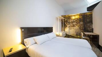 Een moderne hotelkamer met een groot bed, een nachtkastje met een afstandsbediening, een bureau met een stoel en een wanddecoratie met een bosmotief.