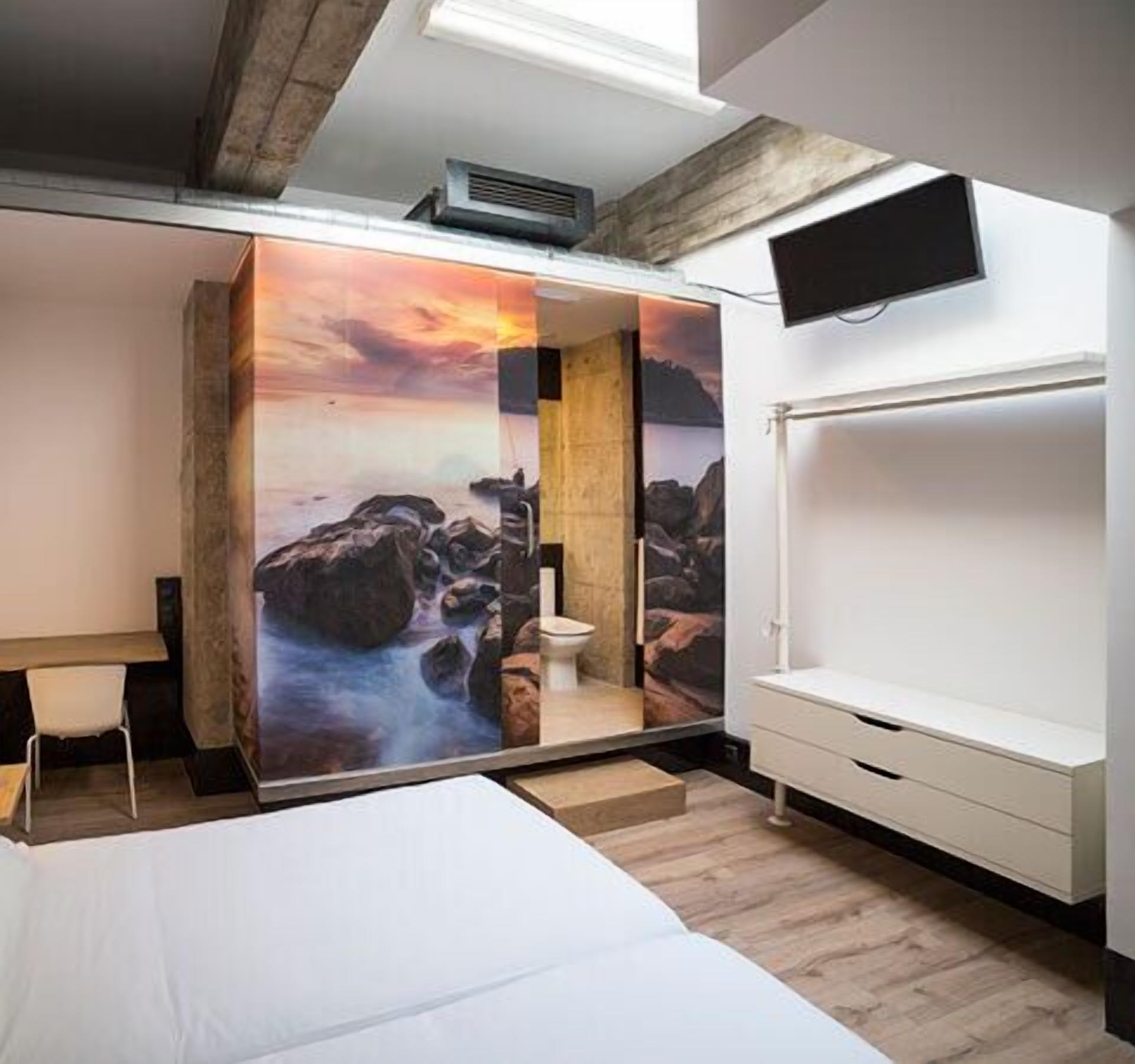 A bedroom with a bed, a desk, and a bathroom with a shower.