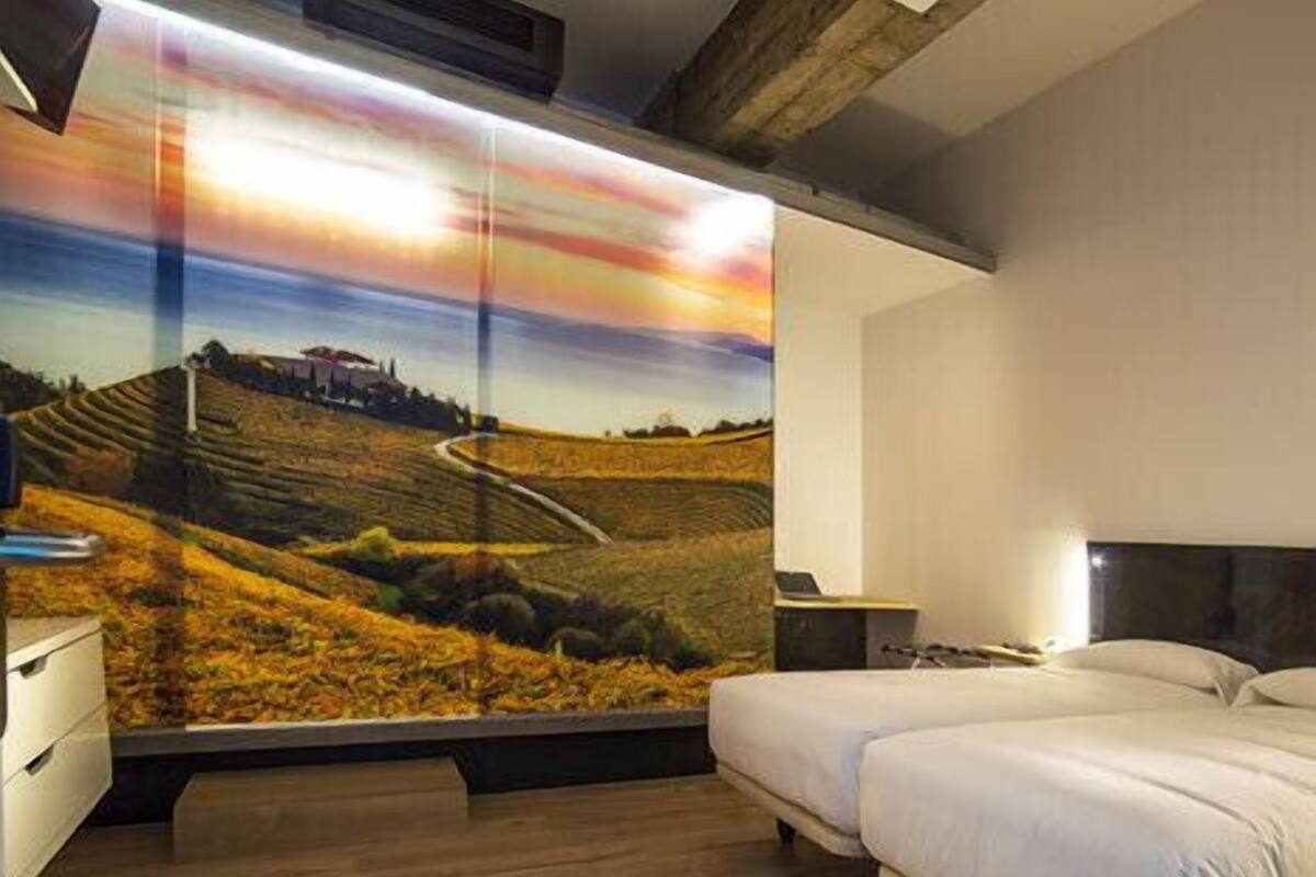 Une chambre avec deux lits, un grand téléviseur fixé au mur qui diffuse un paysage pittoresque, et un plancher en bois.