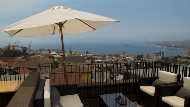 A balcony with outdoor seating, a large umbrella, and a view of the city and sea. - Lofts Magnolio Cerro Alegre (Valparaiso)