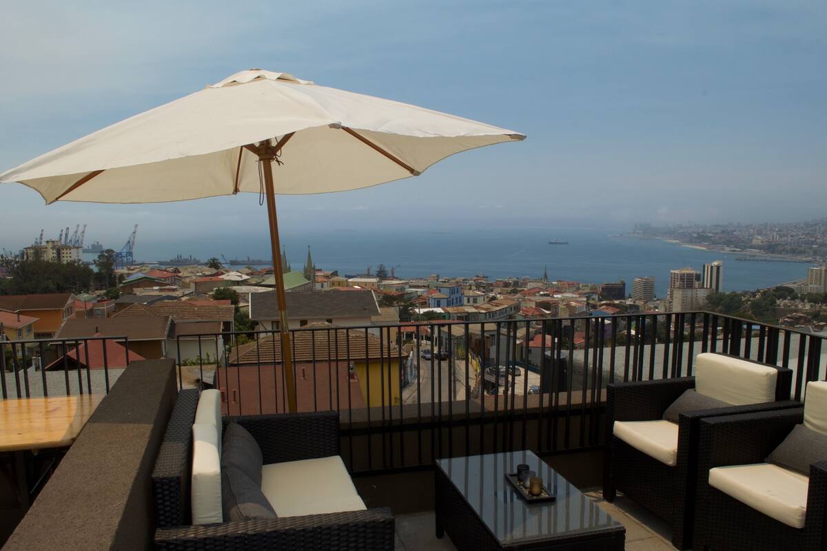 Un balcon avec un espace salon extérieur, un grand parasol et une vue sur la ville et la mer.