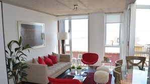 A modern living room with a sofa, red chairs, a glass table, and a large window. - Lofts Magnolio Cerro Alegre (Valparaiso)