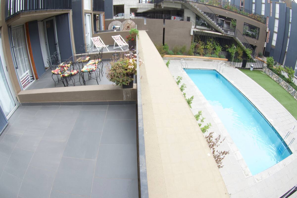Une terrasse sur le toit avec une piscine, des espaces de détente en plein air et une vue sur les bâtiments environnants.