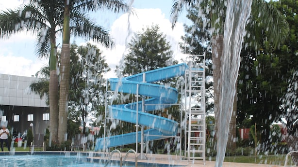 A swimming pool with a blue spiral water slide and palm trees in the background. - Hotel & Resort CIDE (Minga Guazú)