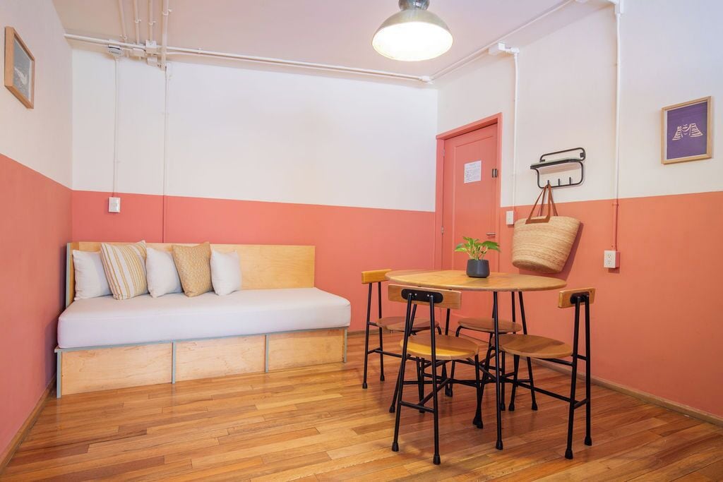Une pièce avec un plancher en bois, un canapé blanc orné de coussins à rayures, une table ronde entourée de quatre chaises et une petite plante en pot.