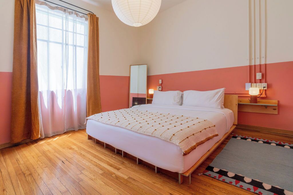 Ein Schlafzimmer mit einem großen Bett, Holzboden, einem Spiegel und einem Nachttisch mit Lampe.