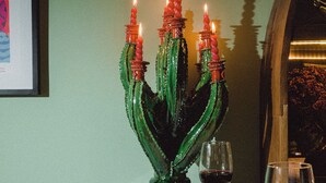 Una mesa de comedor con un centro de mesa de cactus verde, platos de comida, copas de vino y una hogaza de pan.