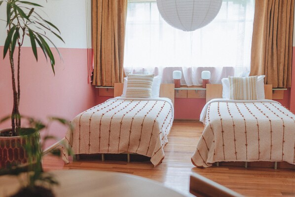 Una habitación con dos camas, una planta en maceta y una ventana con cortinas.