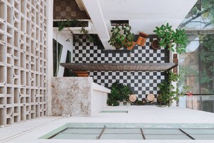 Un espacio exterior moderno con suelo a cuadros, plantas en macetas y un banco de madera.