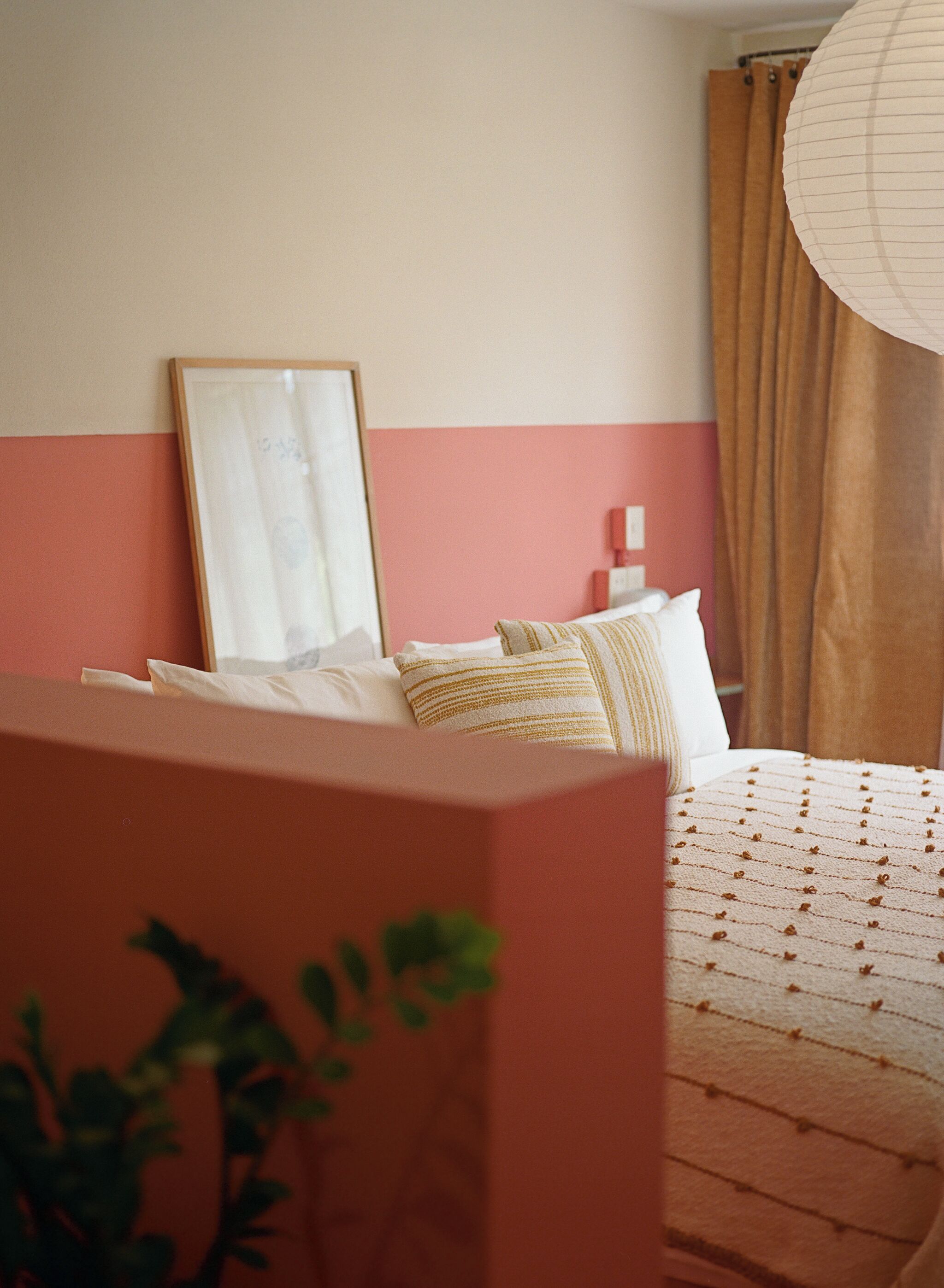 A bedroom with a bed, pillows, a bedside table, a framed picture, and a curtain.