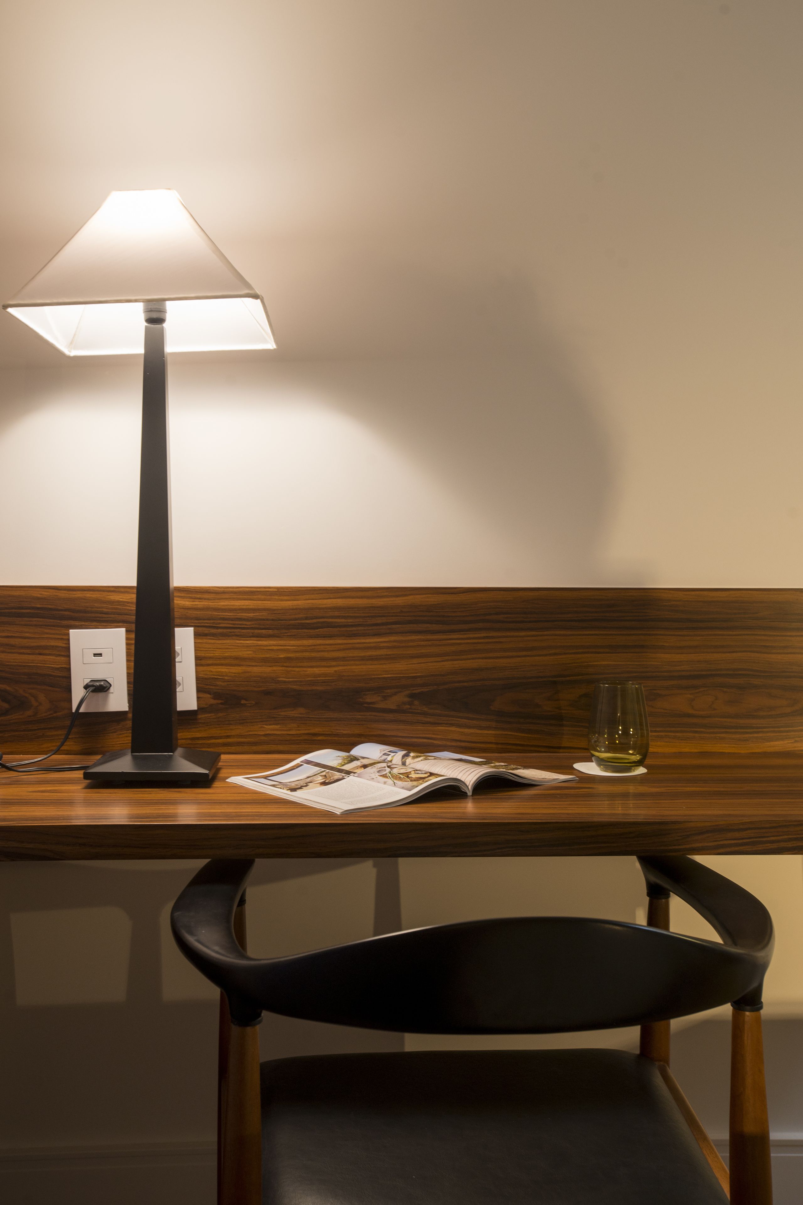 A desk with a lamp, a glass of wine, and a magazine.