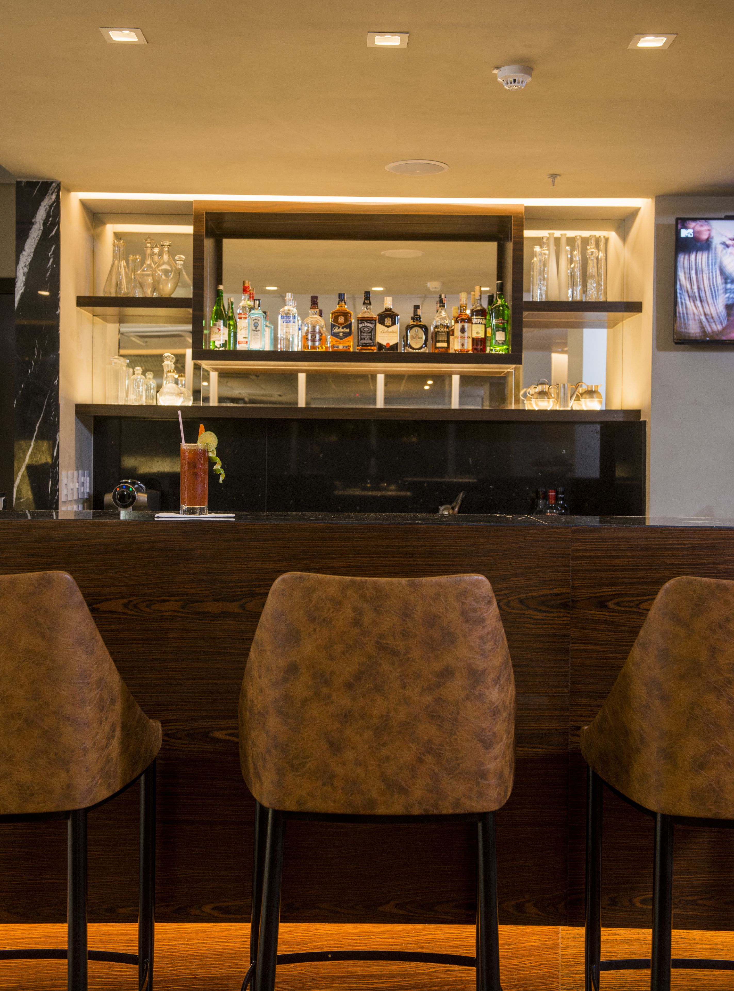 A bar area with a wooden counter, shelves with bottles, and three chairs.