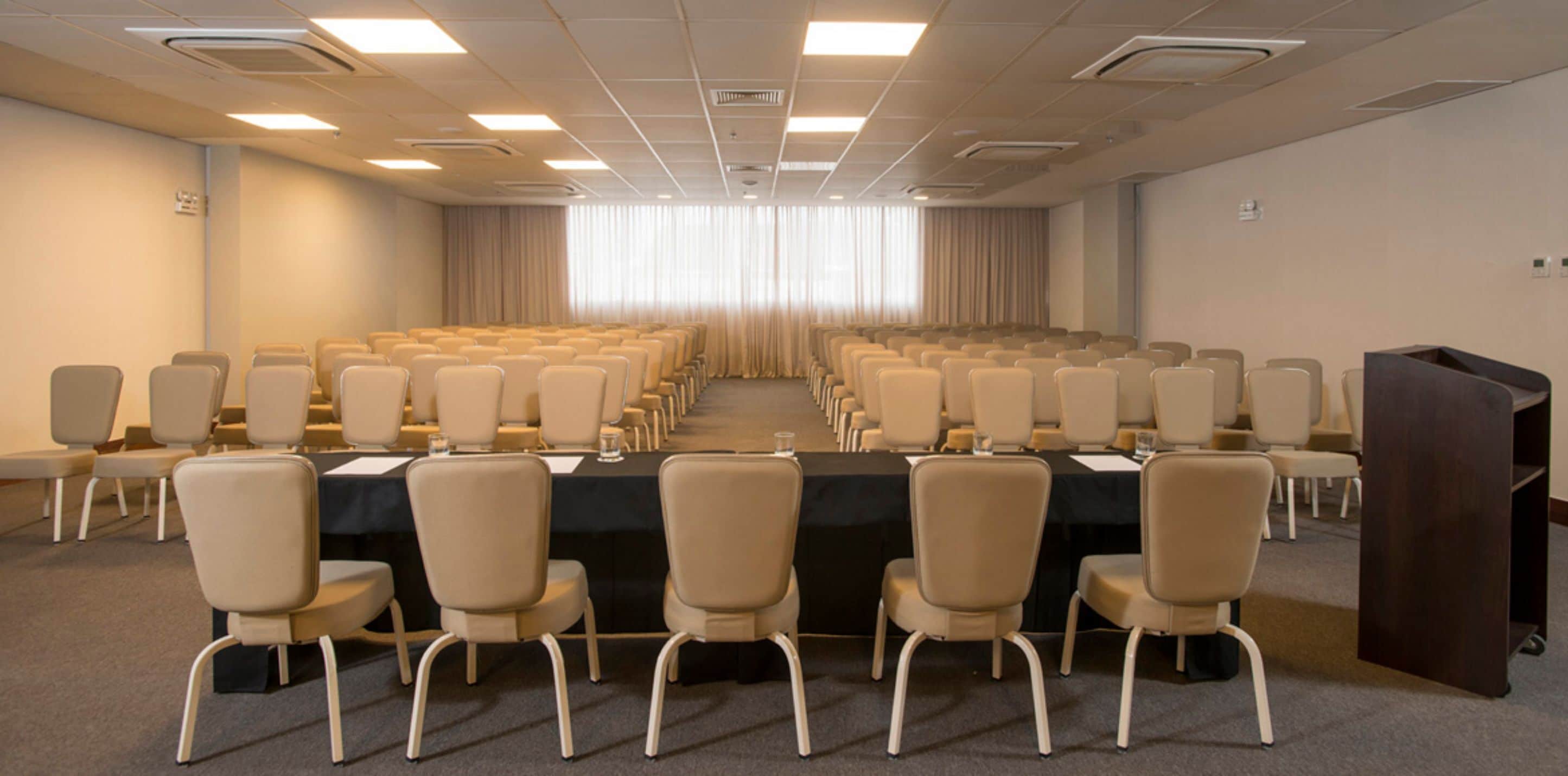 A conference room with rows of chairs, a long table, and a podium.
