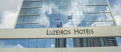 Un edificio de hotel alto con fachada de vidrio moderna y el nombre "Luzieros Hotéis" exhibido en la parte inferior.
