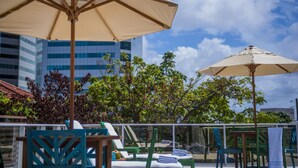 Outdoor seating with umbrellas, a view of trees, and a building in the background. - Hotel Luzeiros Recife (Recife)