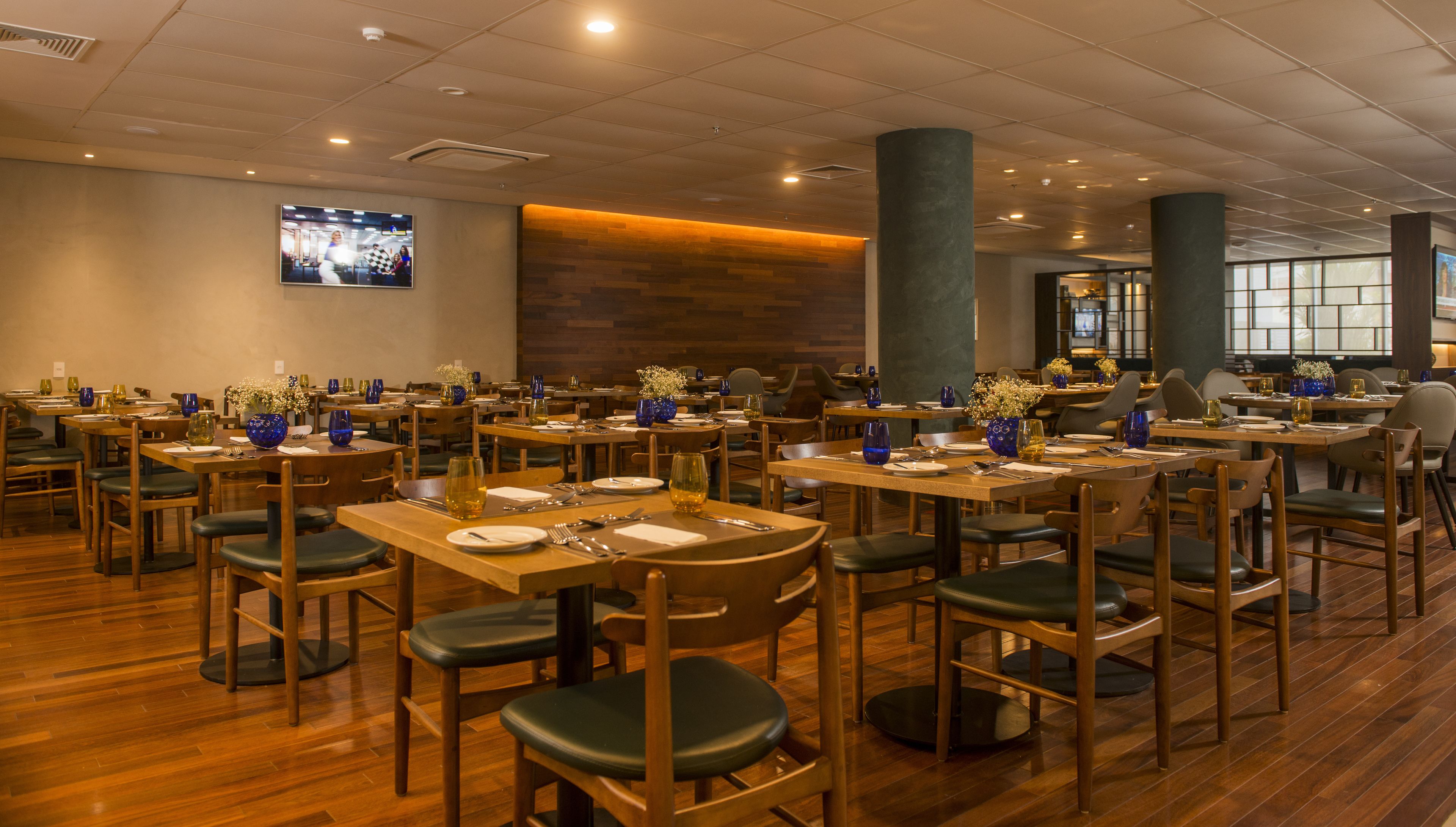 Un restaurant doté de nombreuses tables et chaises, d’un plancher en bois et d’un téléviseur fixé au mur.