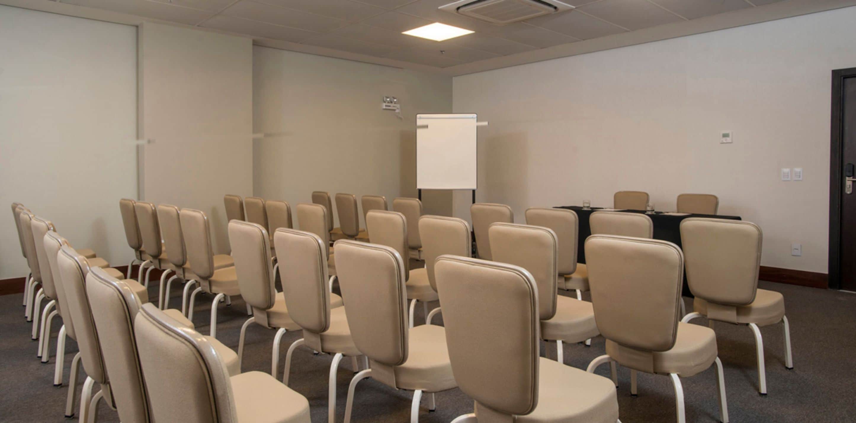 Un salón de conferencias con filas de sillas, una pizarra y una mesa con sillas.