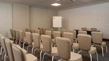 Un salón de conferencias con filas de sillas, una pizarra y una mesa con sillas.