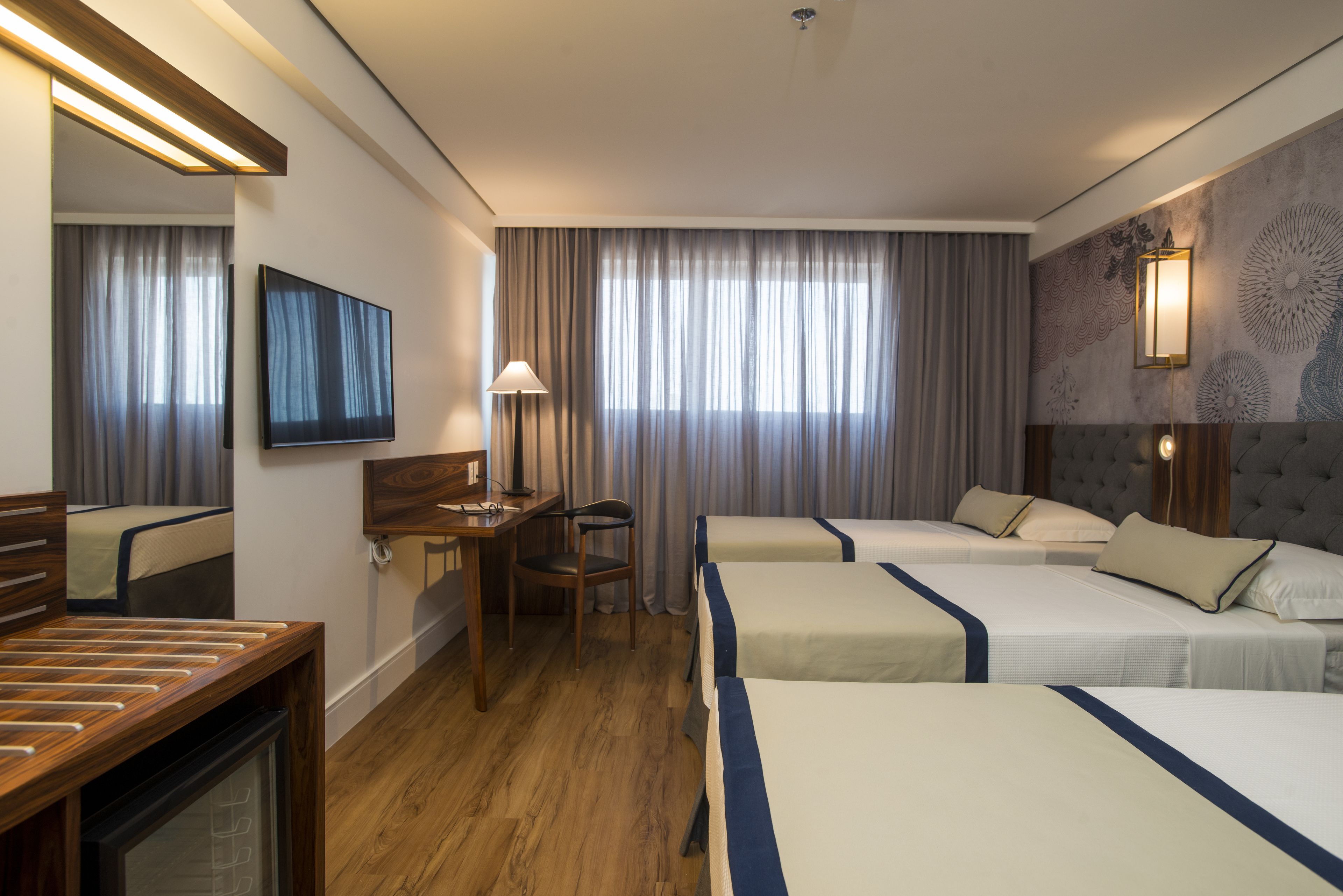 Une chambre d’hôtel avec deux lits, un bureau, une chaise, une télévision et une lampe.